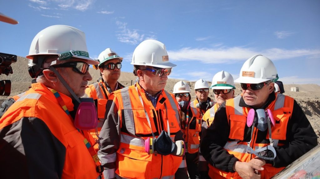Los directores de Codelco visitan Chuquicamata y Radomiro Tomic como parte de una agenda en terreno orientada a conocer las operaciones y fortalecer la seguridad. La delegación estuvo encabezada por el presidente del directorio, Bernardo Fontaine, junto a los nuevos directores Luz Granier, Alejandro Canut de Bon y Daniel Díaz. La visita también contó con la participación del vicepresidente de operaciones (i), Lindor Quiroga, y del presidente ejecutivo, Rubén Alvarado. El recorrido incluyó reuniones con ejecutivos, trabajadores y dirigentes sindicales de ambas divisiones. Seguridad y desempeño marcaron la agenda en Chuquicamata La jornada comenzó en la División Chuquicamata. El equipo ejecutivo liderado por René Galleguillos recibió a la delegación para analizar el estado de la operación y sus principales desafíos. Durante el encuentro, los nuevos directores revisaron indicadores de desempeño y perspectivas de desarrollo. Luego recorrieron la mina subterránea y conocieron procesos vinculados al carguío, transporte y chancado norte. Revisión de controles críticos y proyectos en desarrollo La comitiva visitó además la planta de molienda, el rajo y el Proyecto Domo. En cada área observaron la implementación de controles orientados a prevenir accidentes y fortalecer la gestión de riesgos. Los directores también sostuvieron conversaciones con trabajadores y representantes sindicales. Estos encuentros permitieron recoger opiniones y conocer experiencias desde distintos niveles de la organización. “La seguridad no es sólo una prioridad declarativa, es una responsabilidad permanente que debe reflejarse en cada decisión y en cada tarea”, afirmó Bernardo Fontaine. Radomiro Tomic mostró avances en tecnología e integración operacional En la segunda jornada, los directores de Codelco visitan Chuquicamata y Radomiro Tomic para profundizar su conocimiento sobre los procesos productivos y los desafíos futuros de la Corporación. En Radomiro Tomic, el equipo ejecutivo encabezado por Claudia Domínguez presentó los principales avances de la división. La delegación recorrió instalaciones como el mirador mina, la rotopala, el Proyecto Lixiviación Clorurada y la zona de pilado. Centro Integrado de Operaciones destaca por su aporte tecnológico Uno de los puntos más relevantes fue la visita al Centro Integrado de Operaciones (CIO). Allí conocieron herramientas que permiten optimizar la gestión y coordinar procesos en tiempo real. Los nuevos directores valoraron especialmente el uso de tecnología para mejorar la eficiencia y apoyar la toma de decisiones. Además, destacaron la importancia de integrar procesos para enfrentar los desafíos de la minería moderna. Agenda estratégica para fortalecer el vínculo con las divisiones Las actividades concluyeron con reuniones junto a dirigentes sindicales y equipos ejecutivos. Estas instancias permitieron intercambiar visiones sobre los desafíos operacionales y el futuro de la empresa. Según Fontaine, las visitas en terreno ayudan a comprender mejor la realidad de las operaciones y fortalecen una cultura basada en la responsabilidad compartida. Con este despliegue, el directorio busca consolidar una gestión alineada con cuatro pilares estratégicos. Estos son la seguridad, el aumento de aportes al Estado sin elevar la deuda, la transparencia institucional y la sostenibilidad operacional, económica, ambiental y social de Codelco.